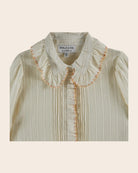 Light-colored blouse with ruffled collar and embroidery on a beige background