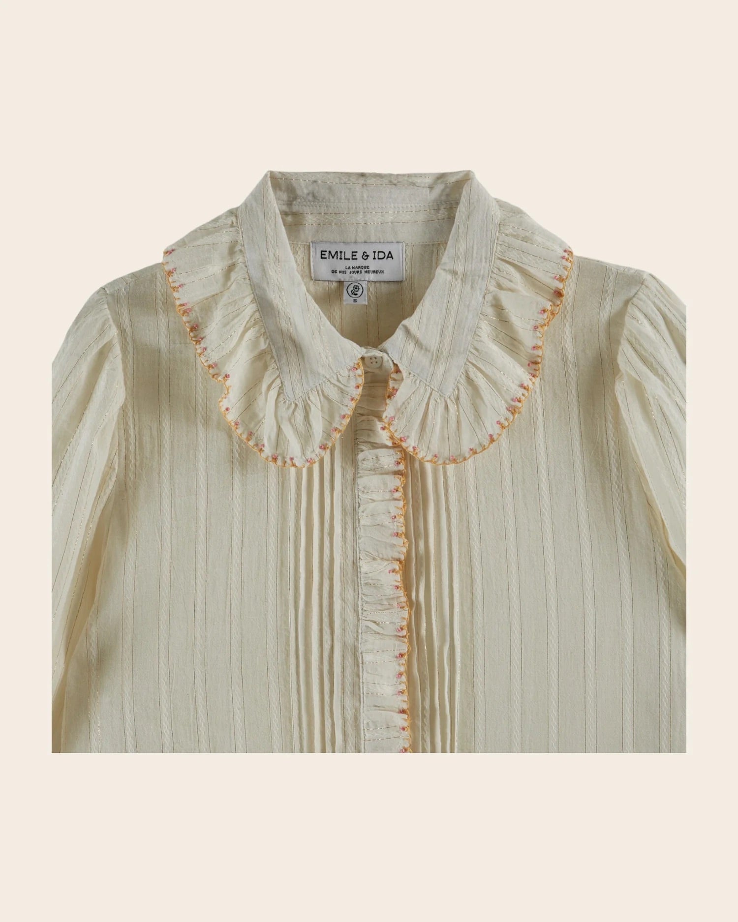 Light-colored blouse with ruffled collar and embroidery on a beige background