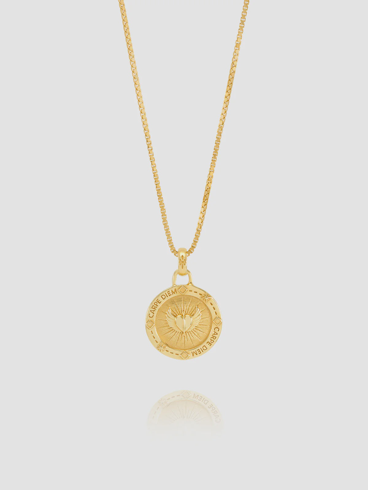 Gold necklace with a circular pendant on a light gray background