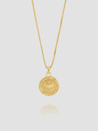 Gold necklace with a circular pendant on a light gray background