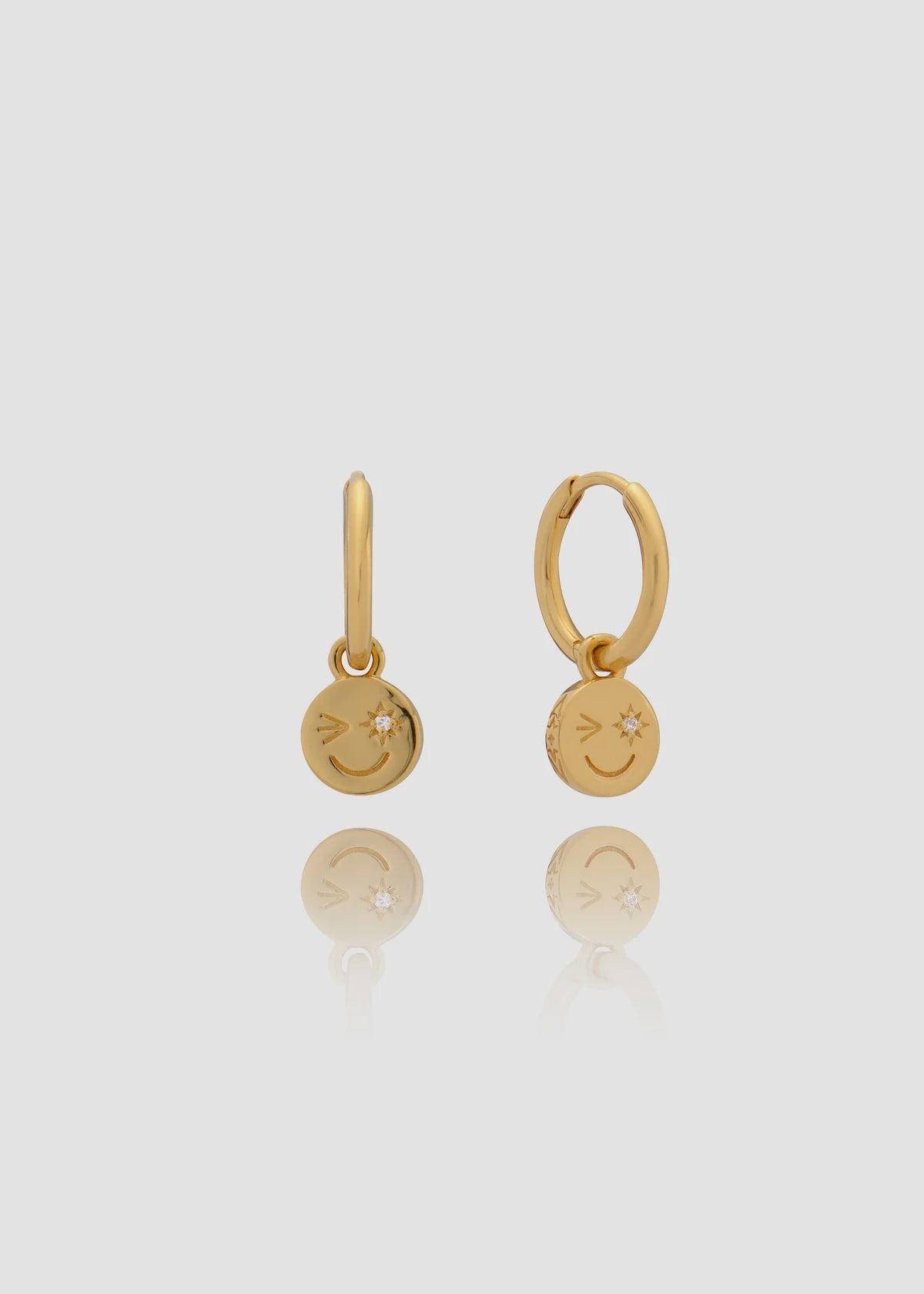 Pair of gold earrings with smiley face charms on a light gray background