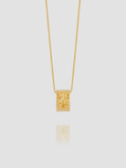 Gold necklace with a cylindrical pendant on a light gray background