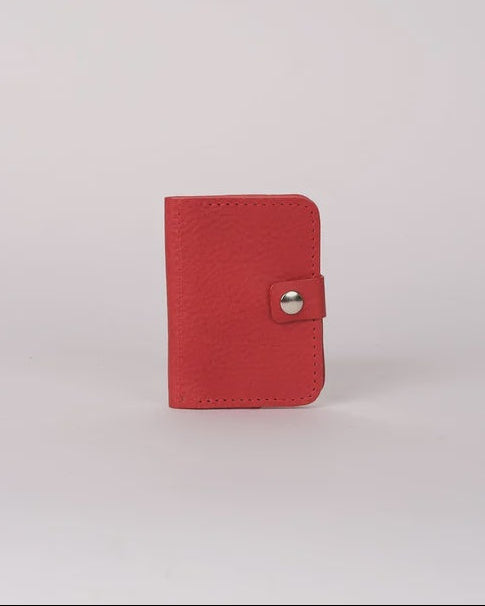 A small red leather card holder or wallet with a snap button closure, standing upright on a light gray background.