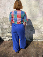 A person standing against a wall wearing cobalt lyocell wide-leg trousers with a flat front waistband, elasticated back, and pleats at the front.