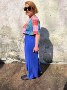 A person standing against a wall wearing cobalt lyocell wide-leg trousers with a flat front waistband, elasticated back, and pleats at the front.
