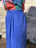 A person standing against a wall wearing cobalt lyocell wide-leg trousers with a flat front waistband, elasticated back, and pleats at the front.