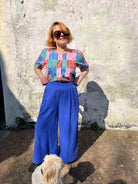 A person standing against a wall wearing cobalt lyocell wide-leg trousers with a flat front waistband, elasticated back, and pleats at the front.