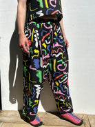 Person wearing colorful abstract pattern pants and pink shoes against a white wall.