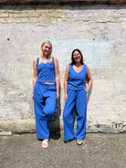 Two women wearing matching blue jumpsuits standing against a textured wall.