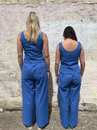 Two people wearing blue jumpsuits standing back-to-back against a textured wall.
