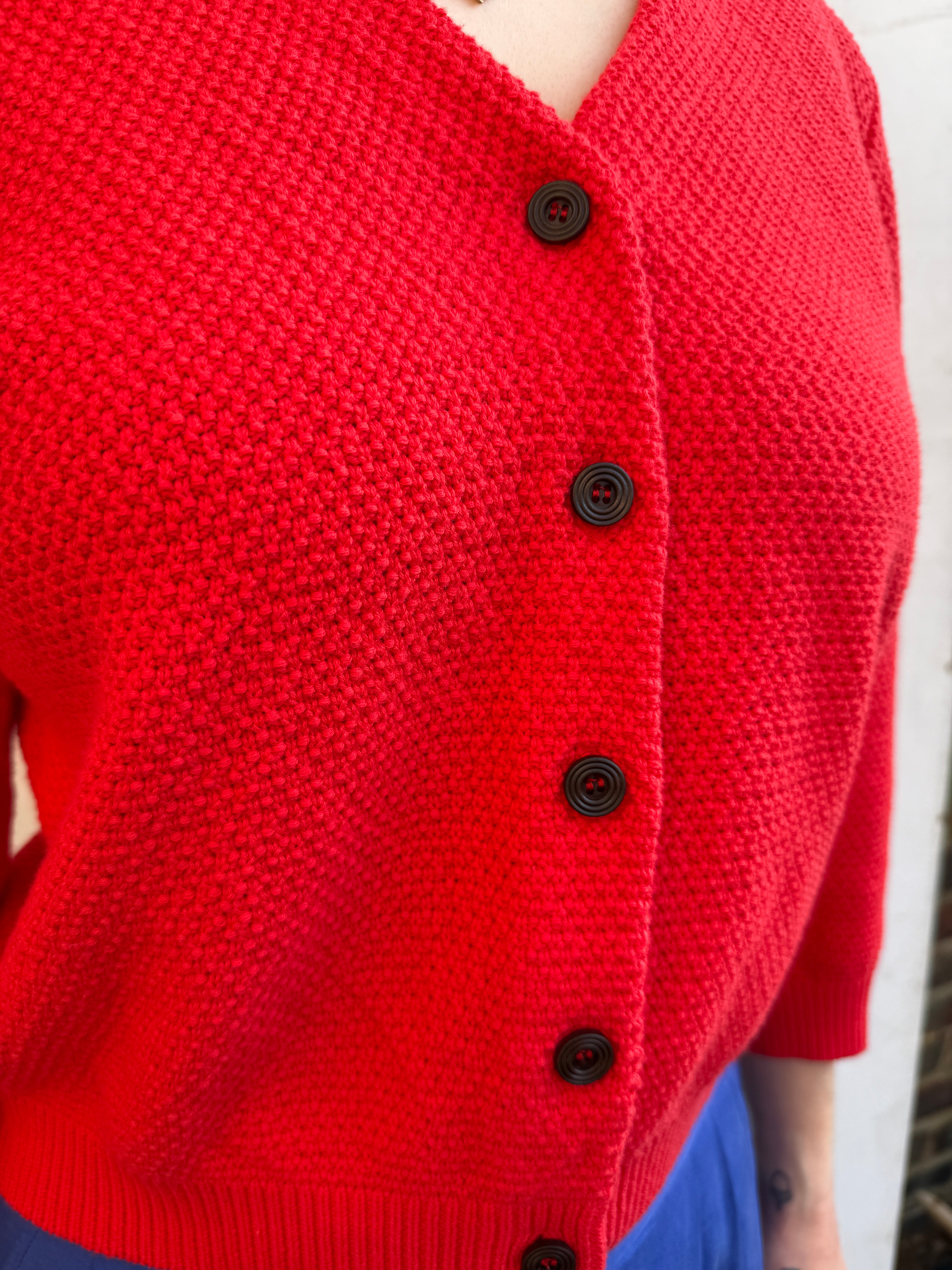 Close-up of a red knitted cardigan with brown buttons on a blurred background
