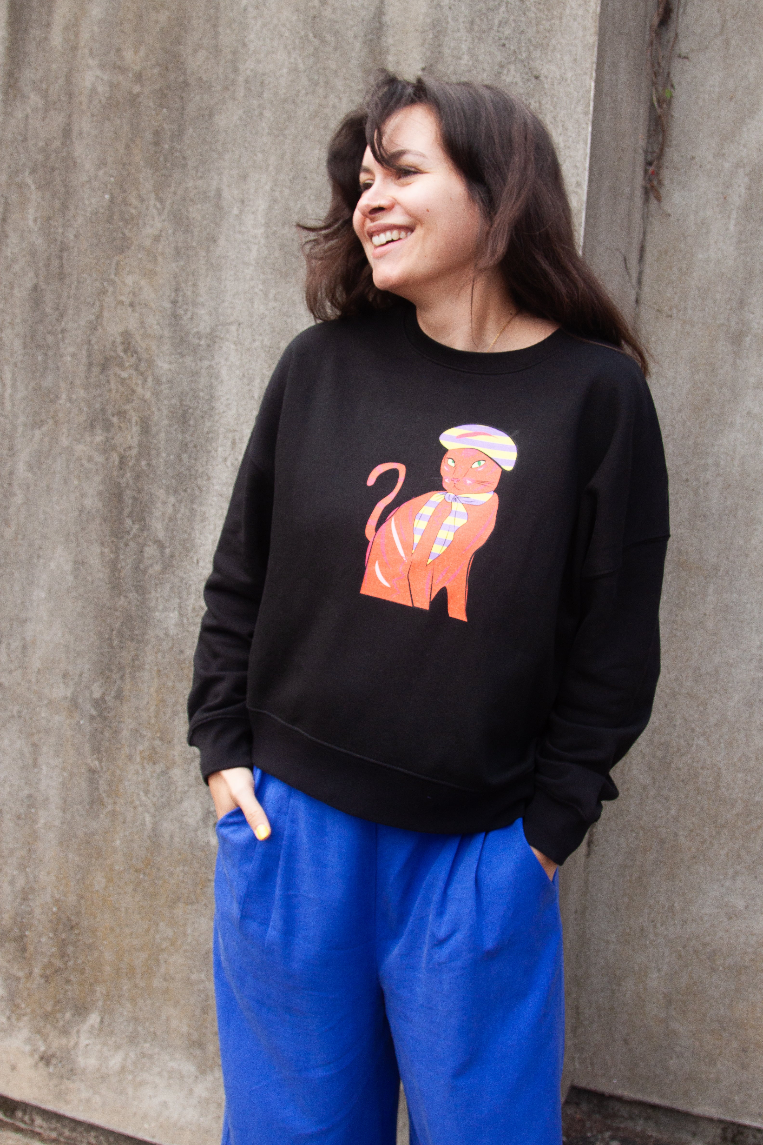 Black sweatshirt with a graphic print of a red and orange cat wearing a Parisian style hat and scarf.