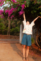 Person in a white shirt and blue shorts standing under a flowering tree with arms outstretched.