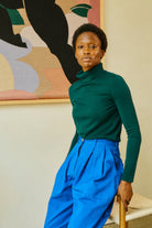 Person wearing a green top and blue pants in a room with abstract art on the wall.