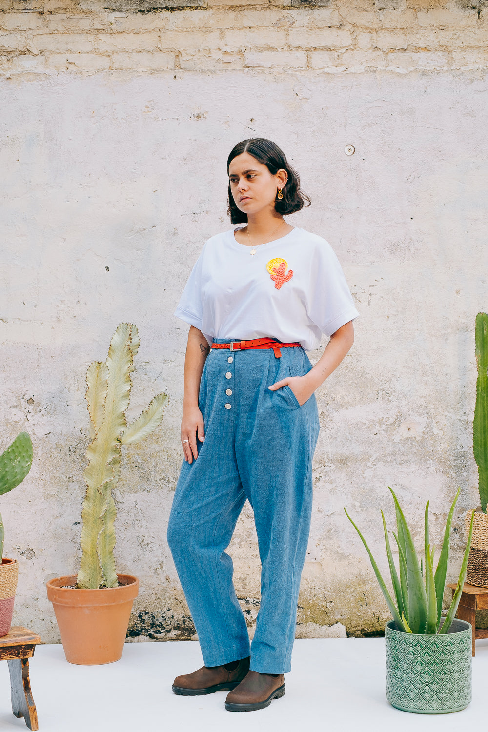 A person wearing a white crew neck t-shirt with a hand-crocheted red and yellow cactus and sun motif, paired with a blue skirt and a red belt.