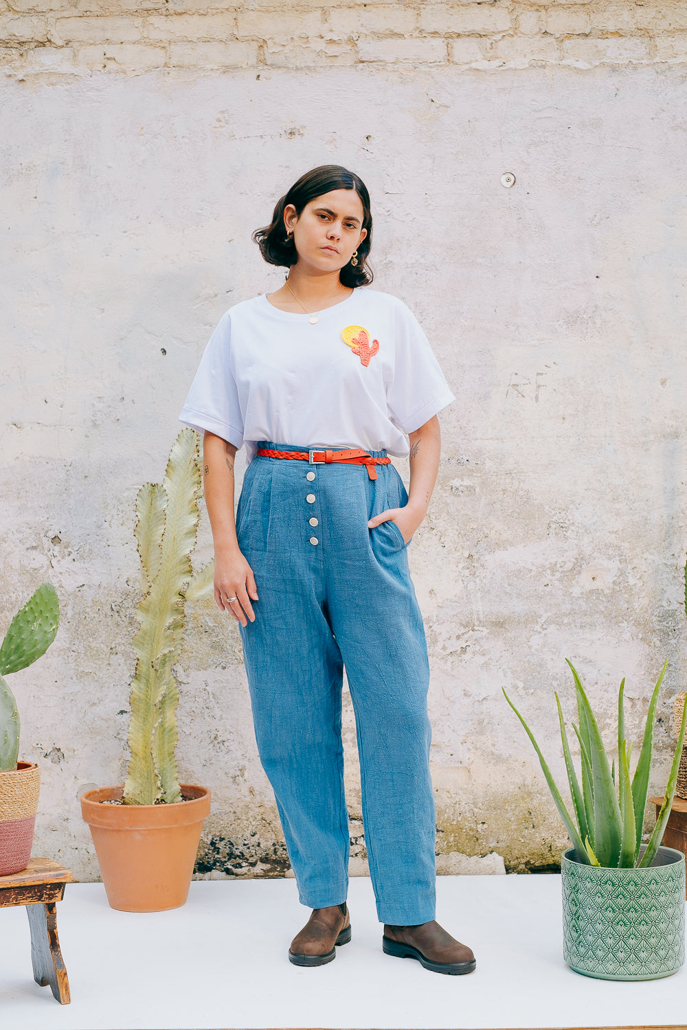 A person wearing a white crew neck t-shirt with a hand-crocheted red and yellow cactus and sun motif, paired with a blue skirt and a red belt.
