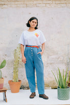 A person wearing a white crew neck t-shirt with a hand-crocheted red and yellow cactus and sun motif, paired with a blue skirt and a red belt.