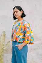 A colorful geometric patterned linen jacket with a V-neckline, elbow length sleeves, and a cropped fit.