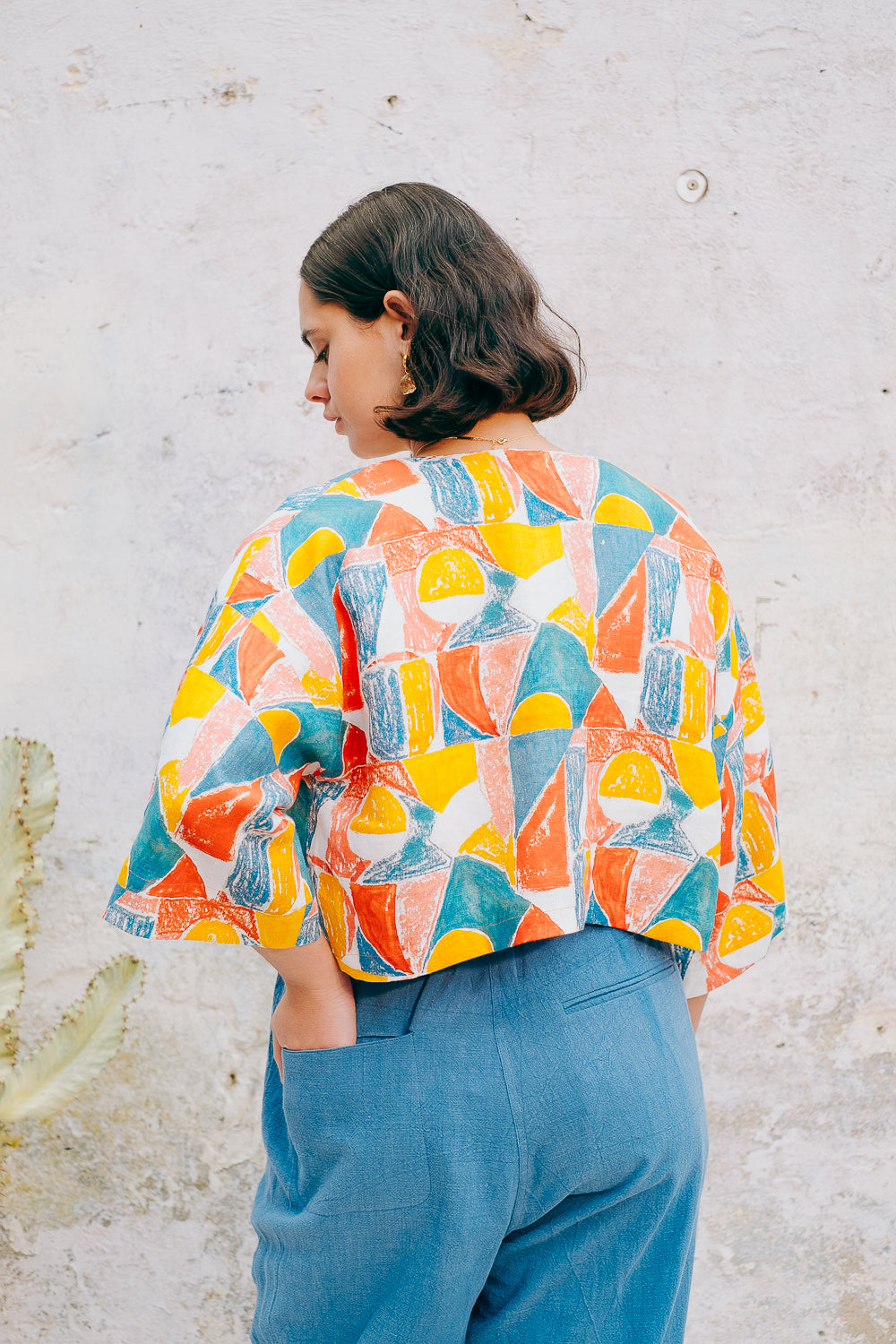 A colorful geometric patterned linen jacket with a V-neckline, elbow length sleeves, and a cropped fit.