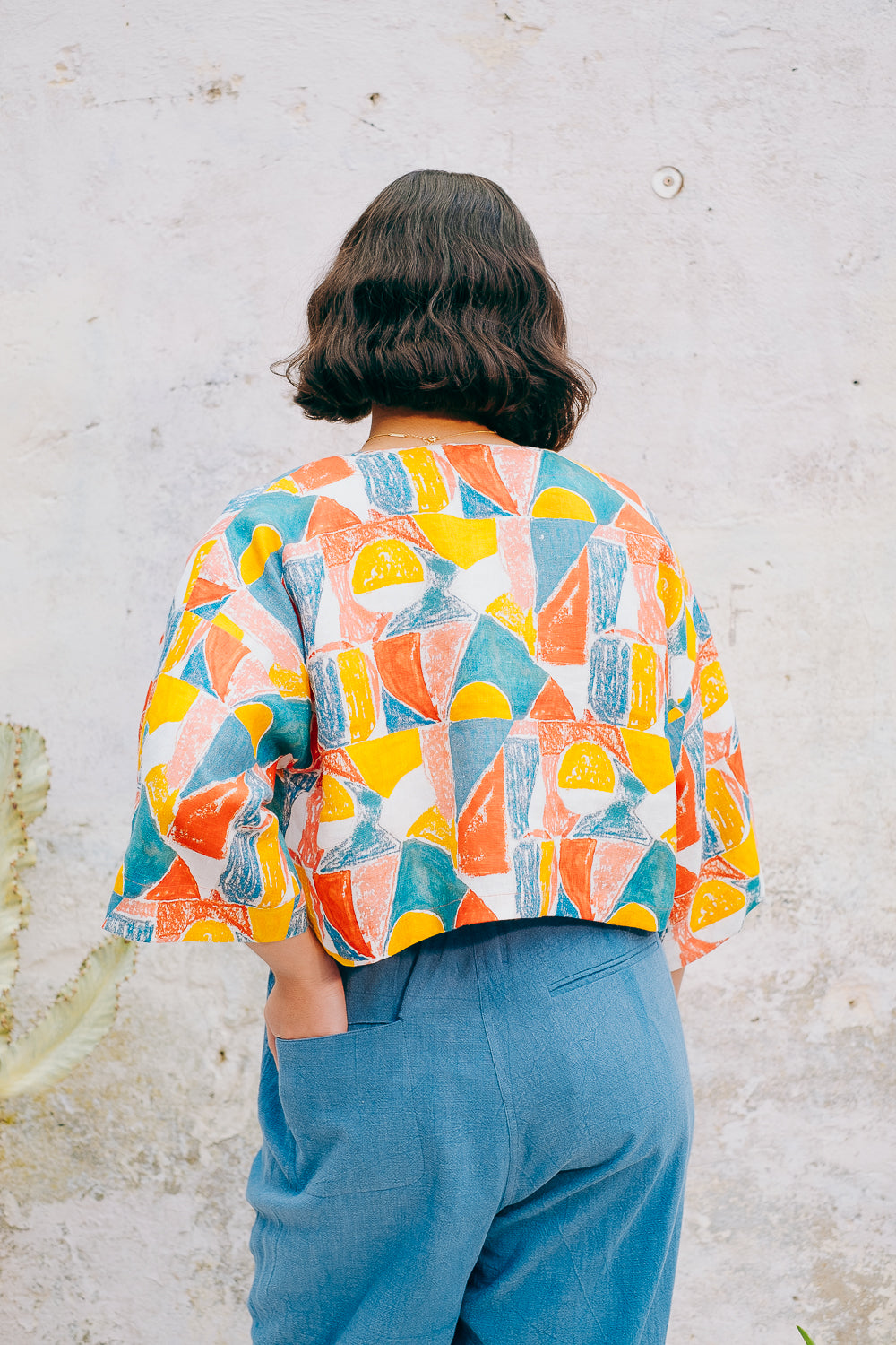 A colorful geometric patterned linen jacket with a V-neckline, elbow length sleeves, and a cropped fit.
