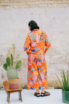 A pair of wide leg cropped trousers with a desert print in vibrant bright orange, featuring front pleats, an elasticated back waist, button and zip on the side, and side pockets.