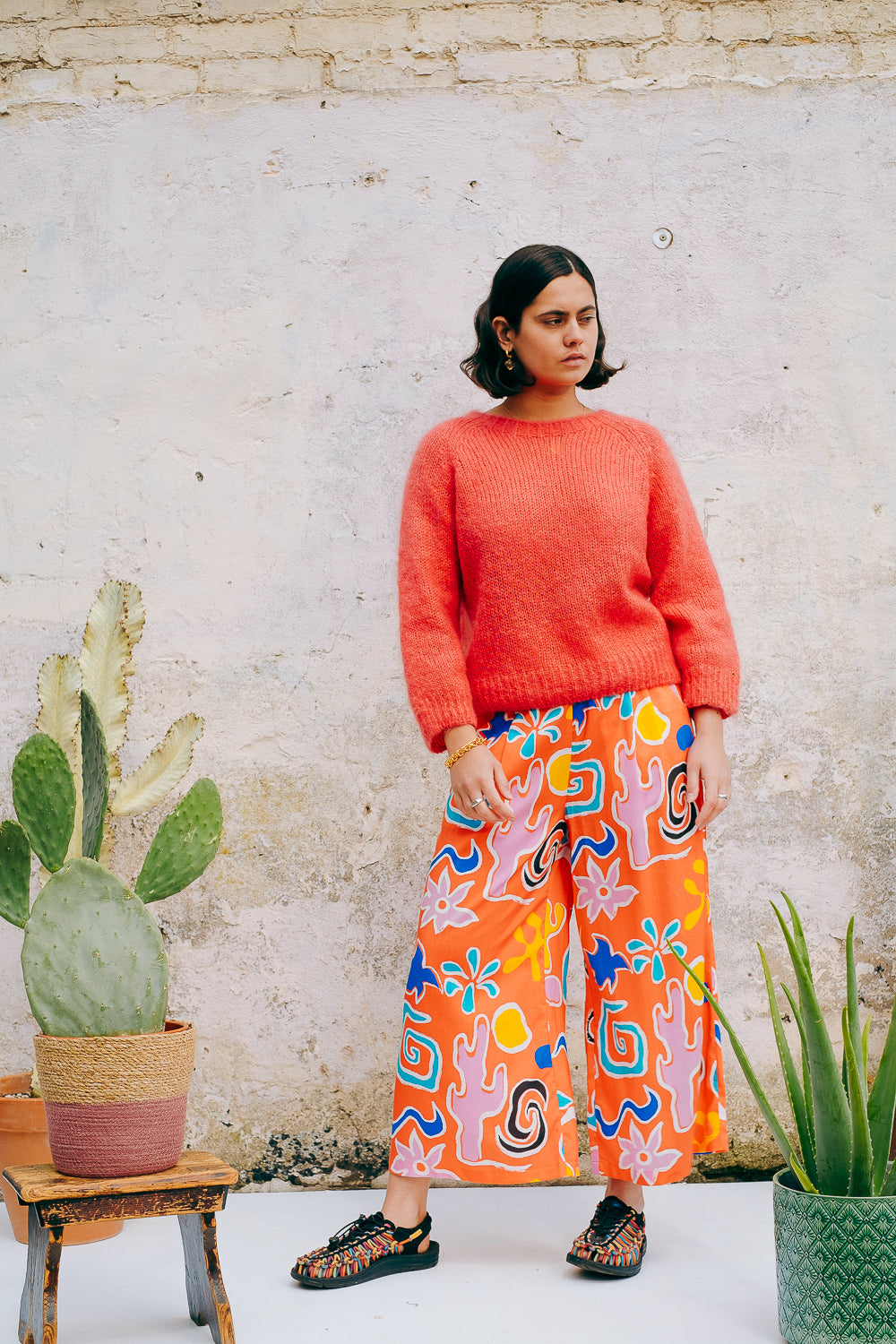 A pair of wide leg cropped trousers with a desert print in vibrant bright orange, featuring front pleats, an elasticated back waist, button and zip on the side, and side pockets.