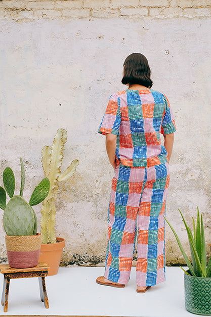 A pair of straight leg trousers with a multicolored grid check pattern. The trousers have a flat front, elasticated waist at the back, and side patch pockets.