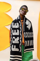 Person wearing a black and white patterned scarf with 'FREE' text, standing against a yellow and beige background.