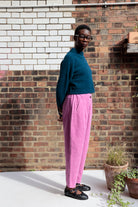 Person wearing a teal sweater and pink pants standing against a brick wall.