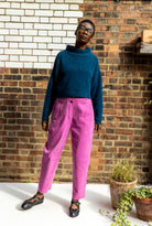 Person wearing a blue sweater and pink pants standing against a brick wall.
