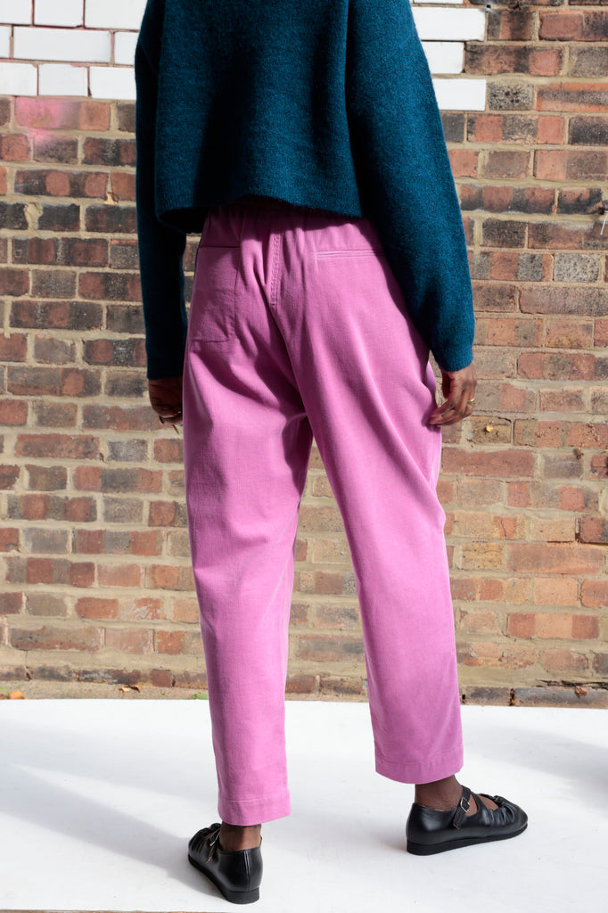 Person wearing pink pants and a blue sweater standing against a brick wall.
