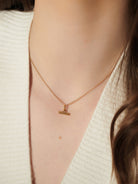 Gold necklace with a small pendant worn by a person against a neutral background