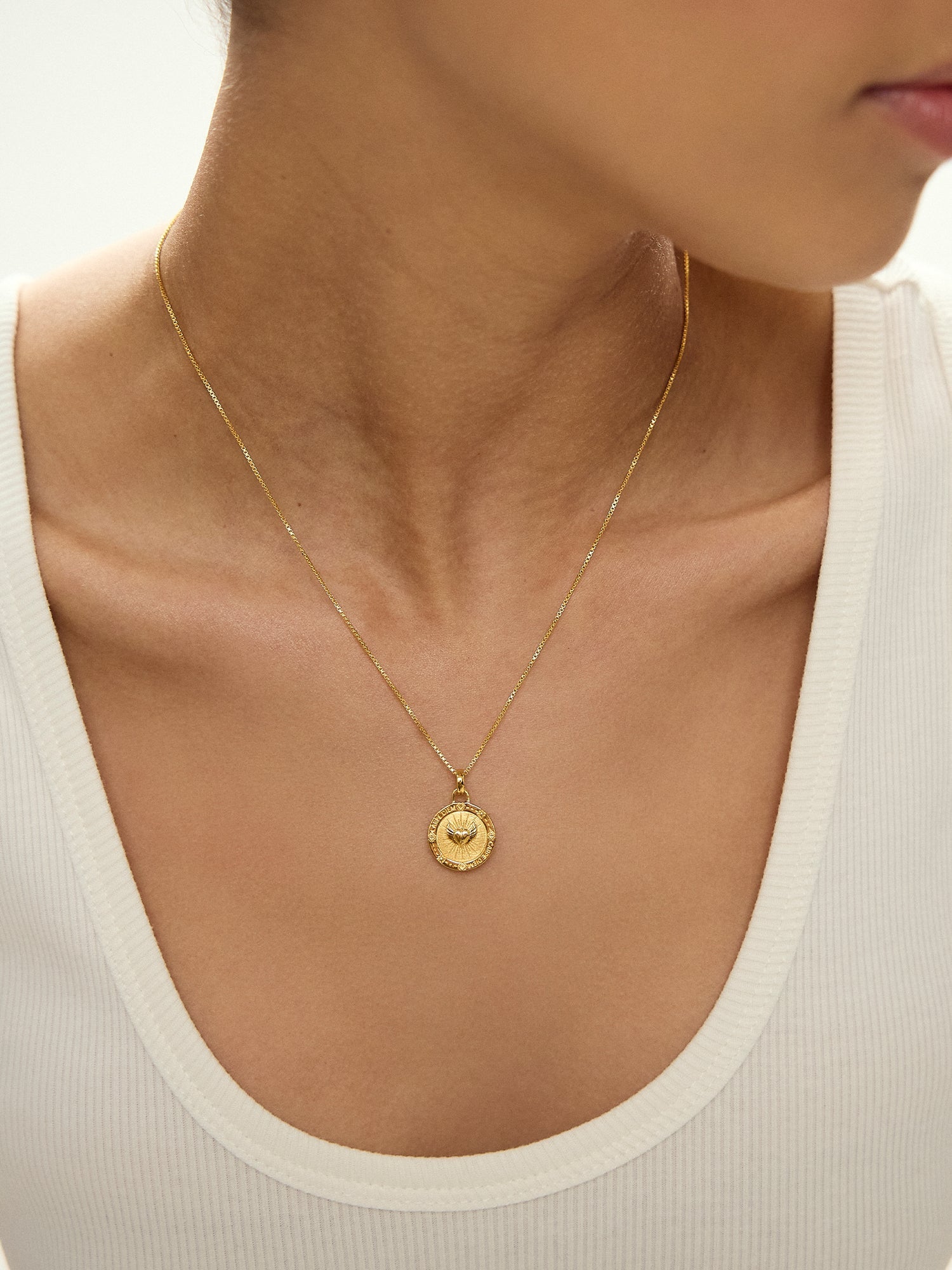 Gold necklace with a pendant on a person wearing a white top