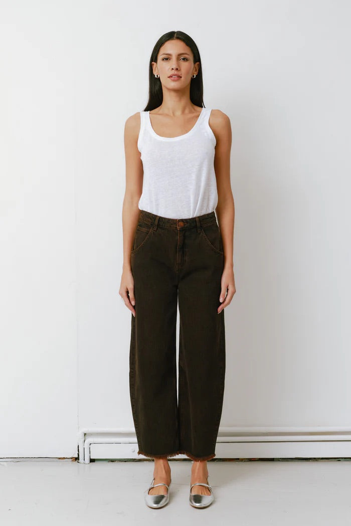 Woman wearing a white tank top and dark pants against a white background