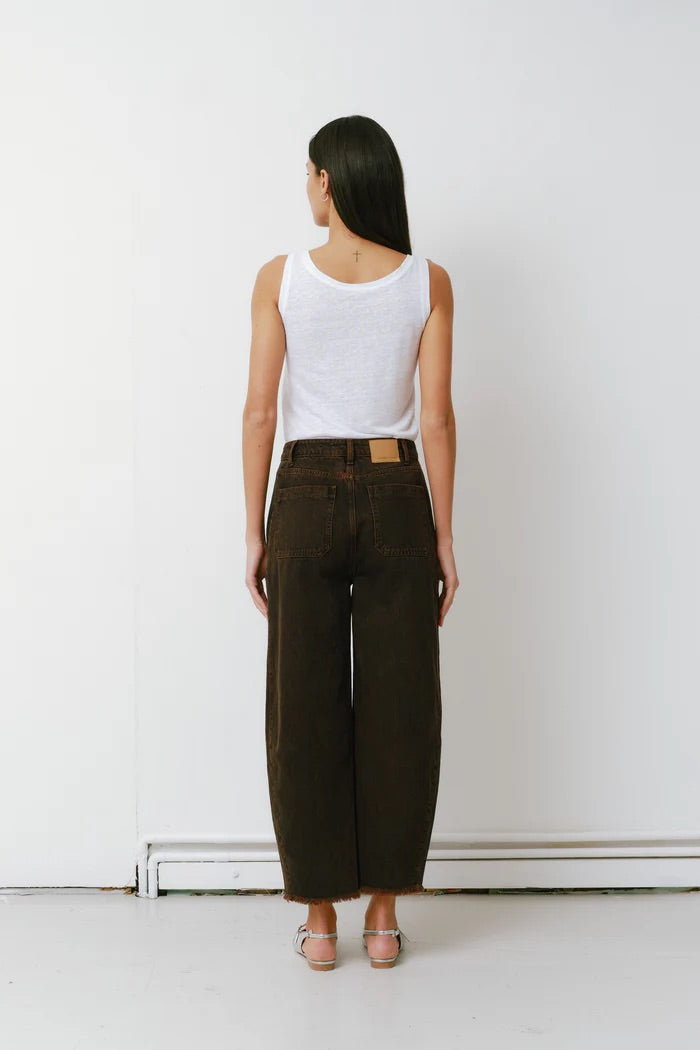 Person wearing a white tank top and dark green wide-leg pants against a white wall.