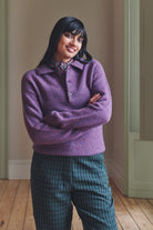 Woman wearing a purple sweater and green plaid pants standing indoors.