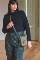 Woman holding a green crossbody bag in an indoor setting