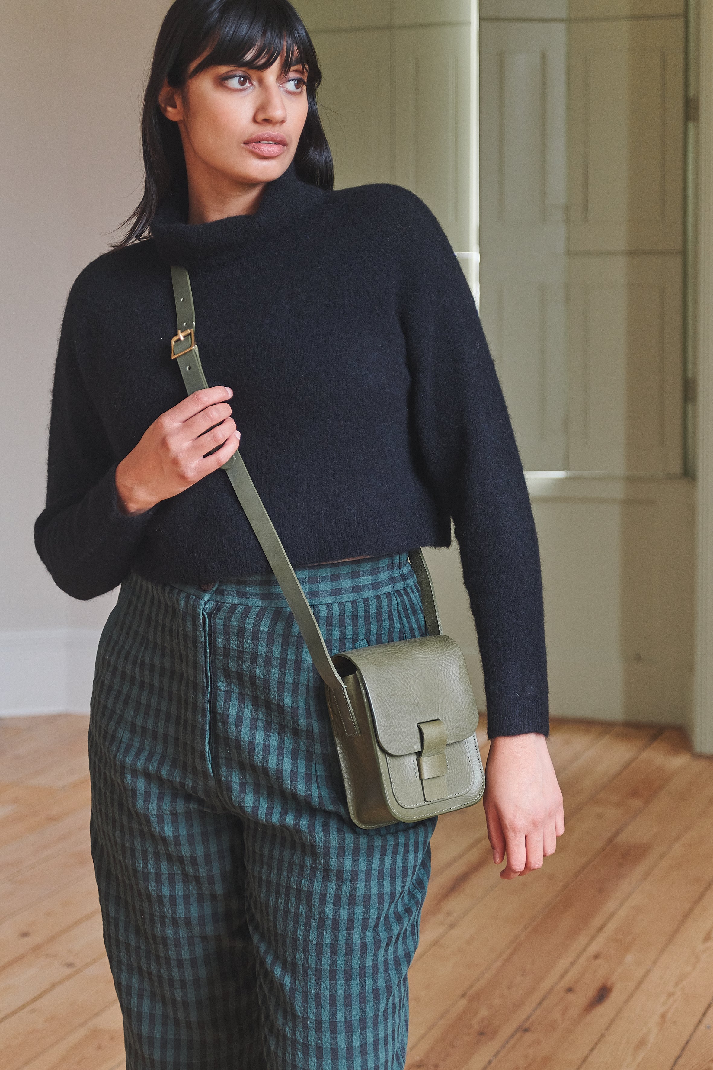 Woman holding a green crossbody bag in an indoor setting
