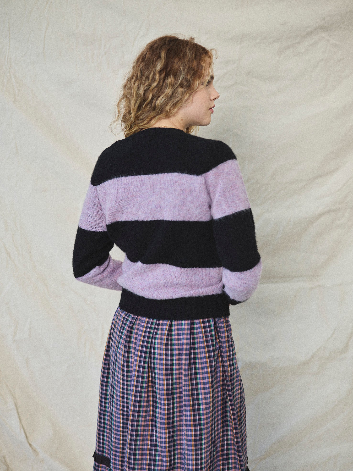 A striped Scottish jumper with horizontal black and lilac blocks, featuring a round neckline and ribbed-knit hemline and trim around neck and wrist.