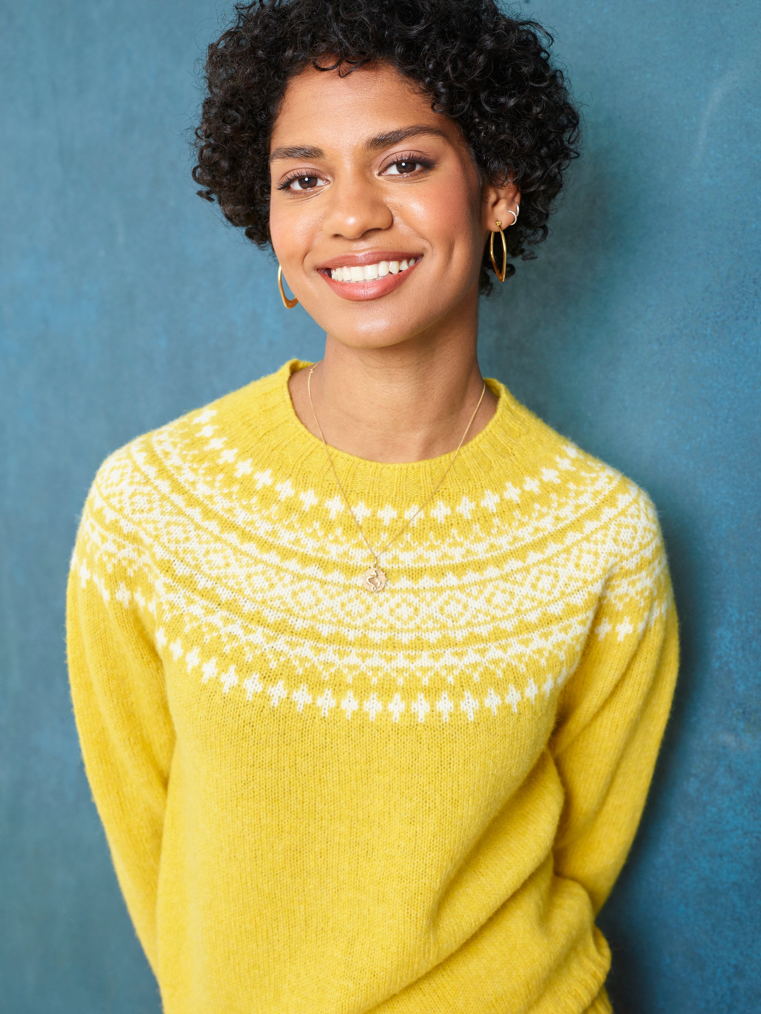 Woman wearing a yellow sweater with white patterns against a blue background