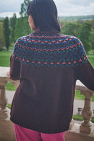 Person wearing a patterned sweater standing on a stone balcony with a scenic view.