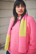 Person wearing a pink sweater with a yellow scarf against a neutral background