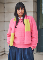 Person wearing a pink sweater with a yellow scarf in an urban setting
