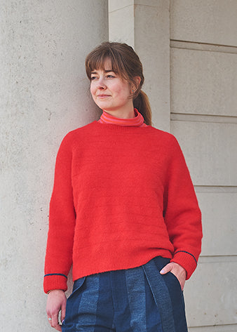 Woman wearing a red sweater standing against a light-colored wall.
