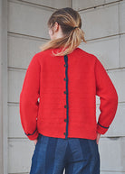Person wearing a red cardigan with black buttons against a light gray wall.