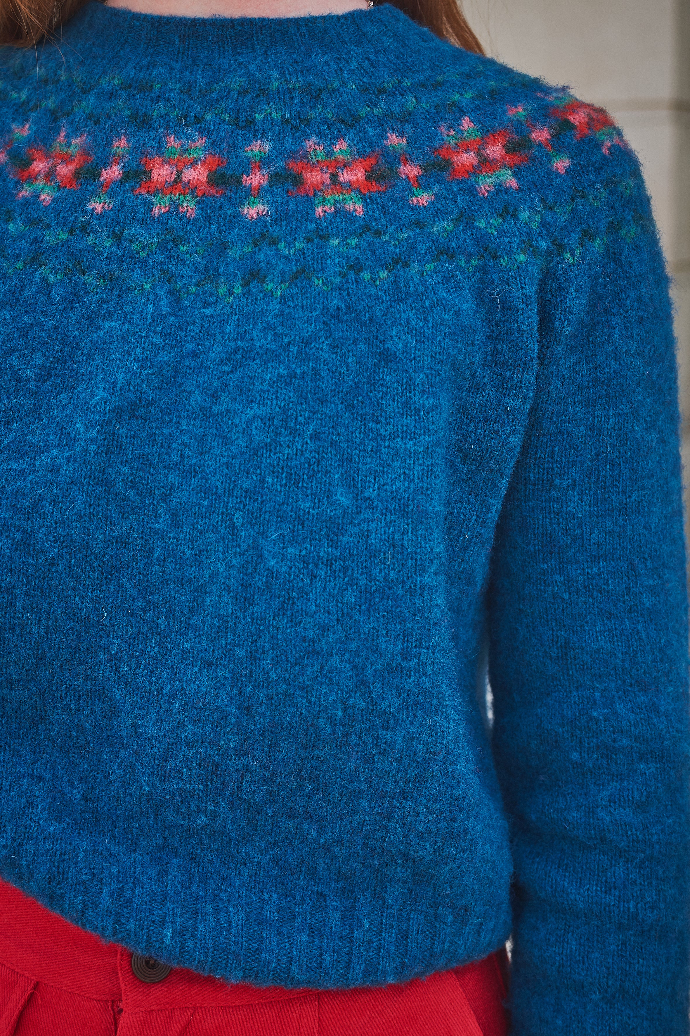 Blue knitted sweater with floral patterns on the shoulders against a neutral background