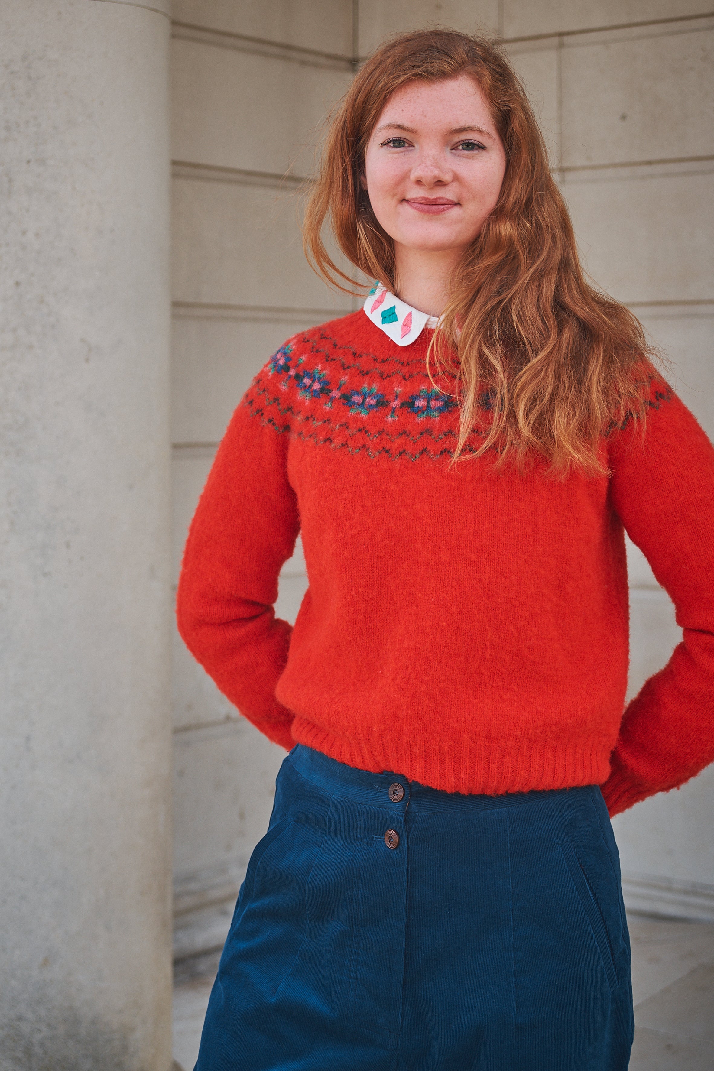 Person wearing a red sweater with a pattern, standing against a light-colored wall.