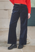 Person wearing navy pants and a red top standing against a stone wall.