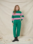 Woman wearing a green and pink striped sweater with green pants against a beige background