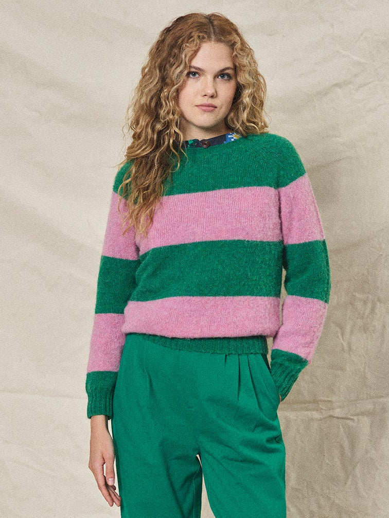 Woman wearing a green and pink striped sweater with green pants against a beige background